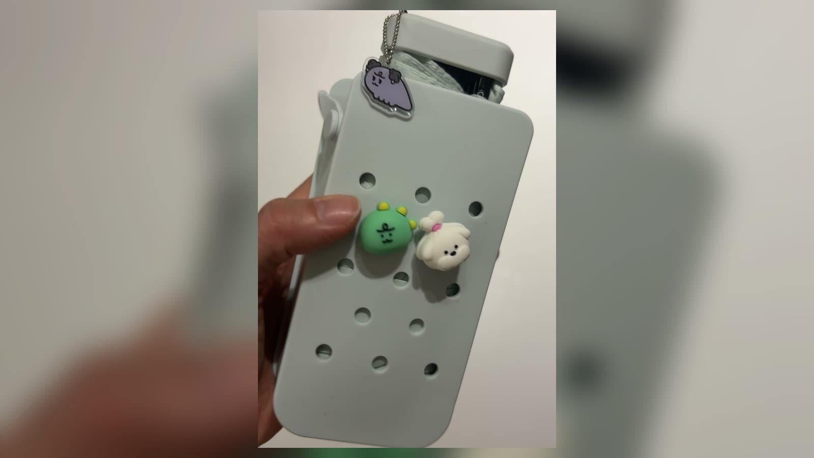 A hand holding Daiso's mint silicone-pouch folding umbrella decorated with Crocs-style character charms and an acrylic keyring
