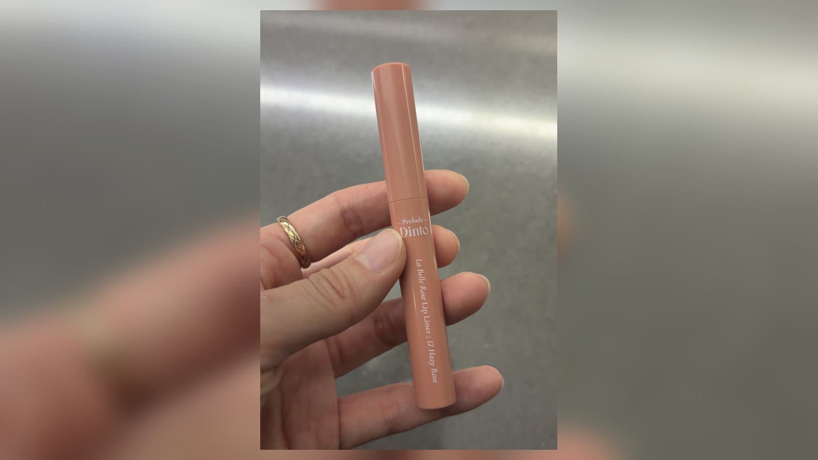 Prelude Dinto La Belle Rose lip liner in shade 12 Hazy Rose held in hand, a slim peach-pink pencil